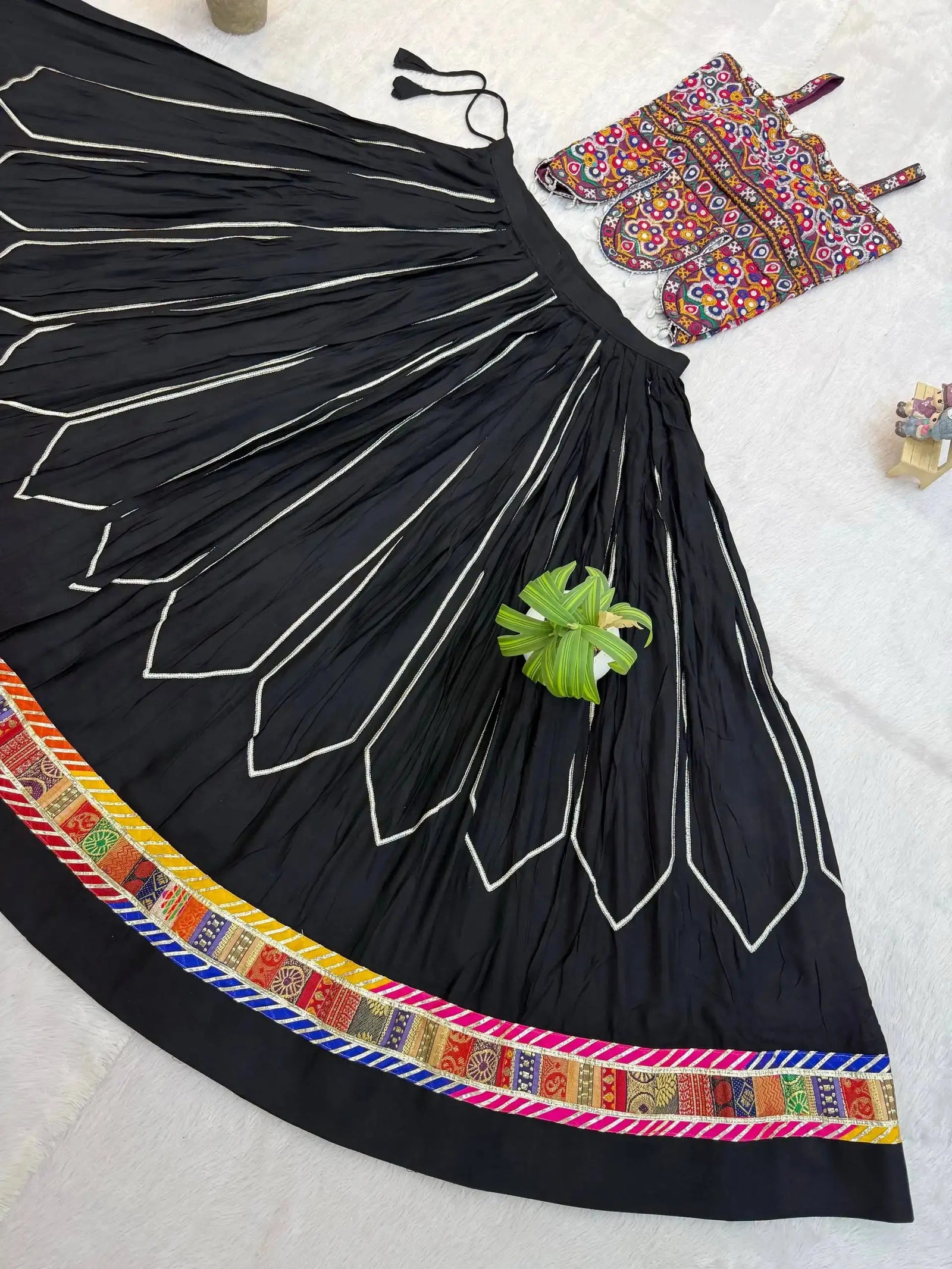 Flat lay detail of black circular lehenga skirt showing white chevron embroidery and colorful patola border