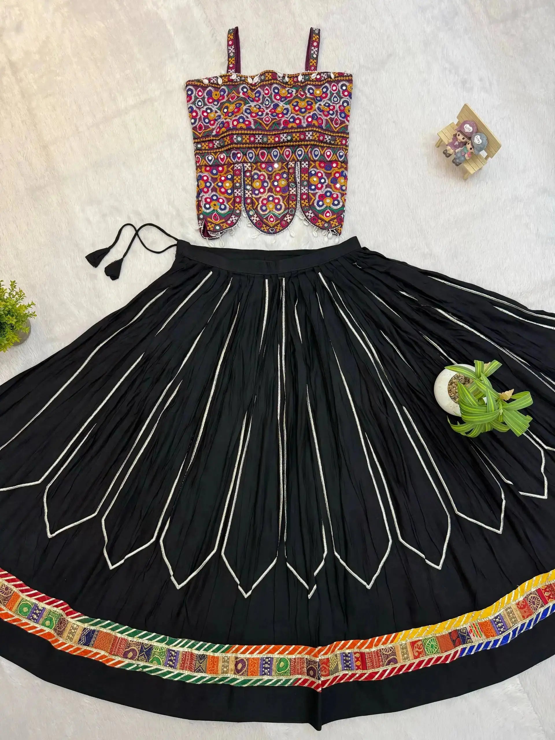 Flat lay of black heavy embroidered lehenga set with multicolor Kutchi choli and circular skirt