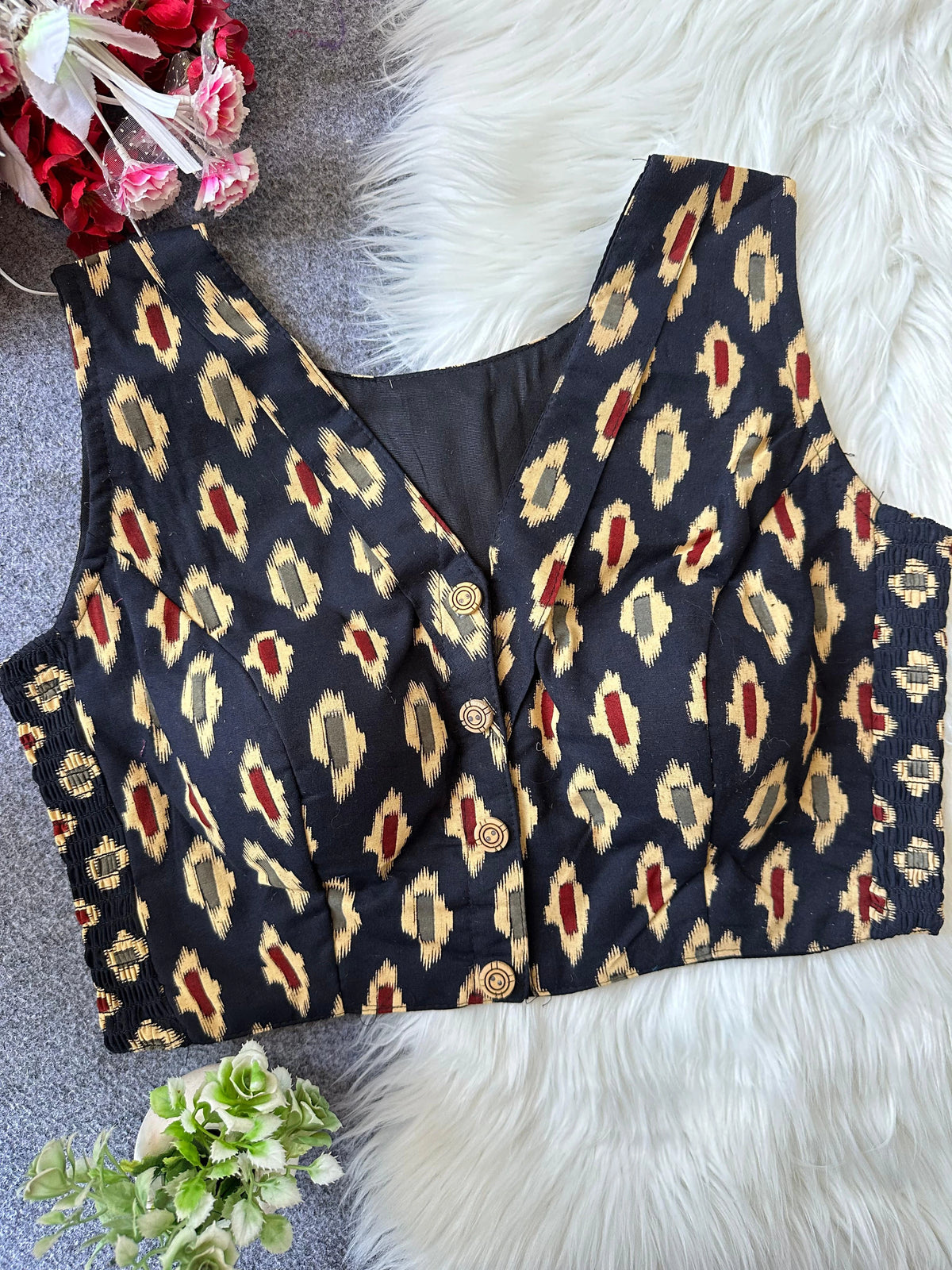 Black patterned vest on a textured surface with flowers and greenery.