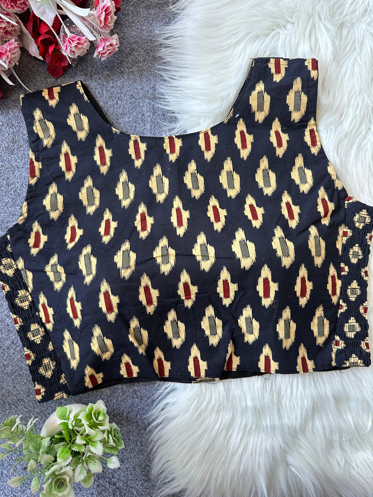 Black patterned top on a textured surface with flowers and fur.
