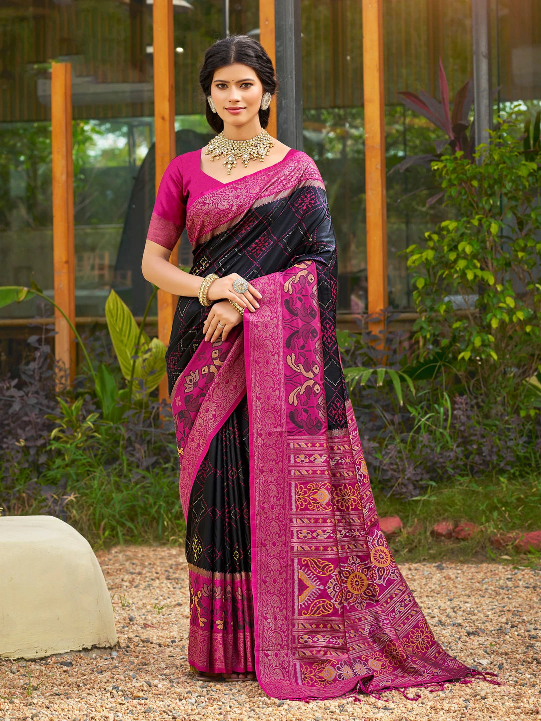 Woman wearing a black and pink saree with a garden background