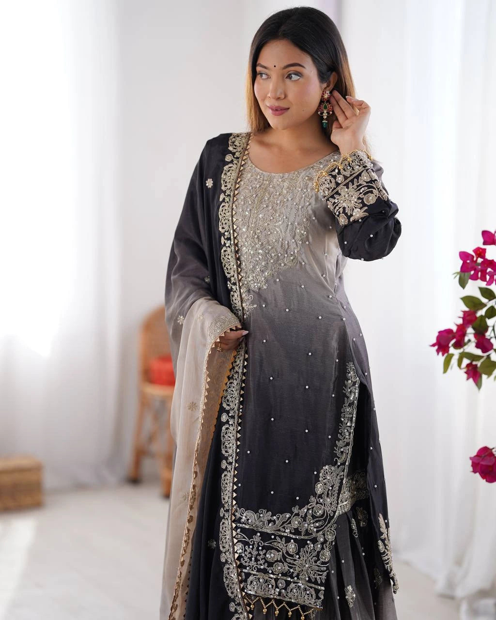 Woman wearing a traditional outfit with intricate designs in a bright room.