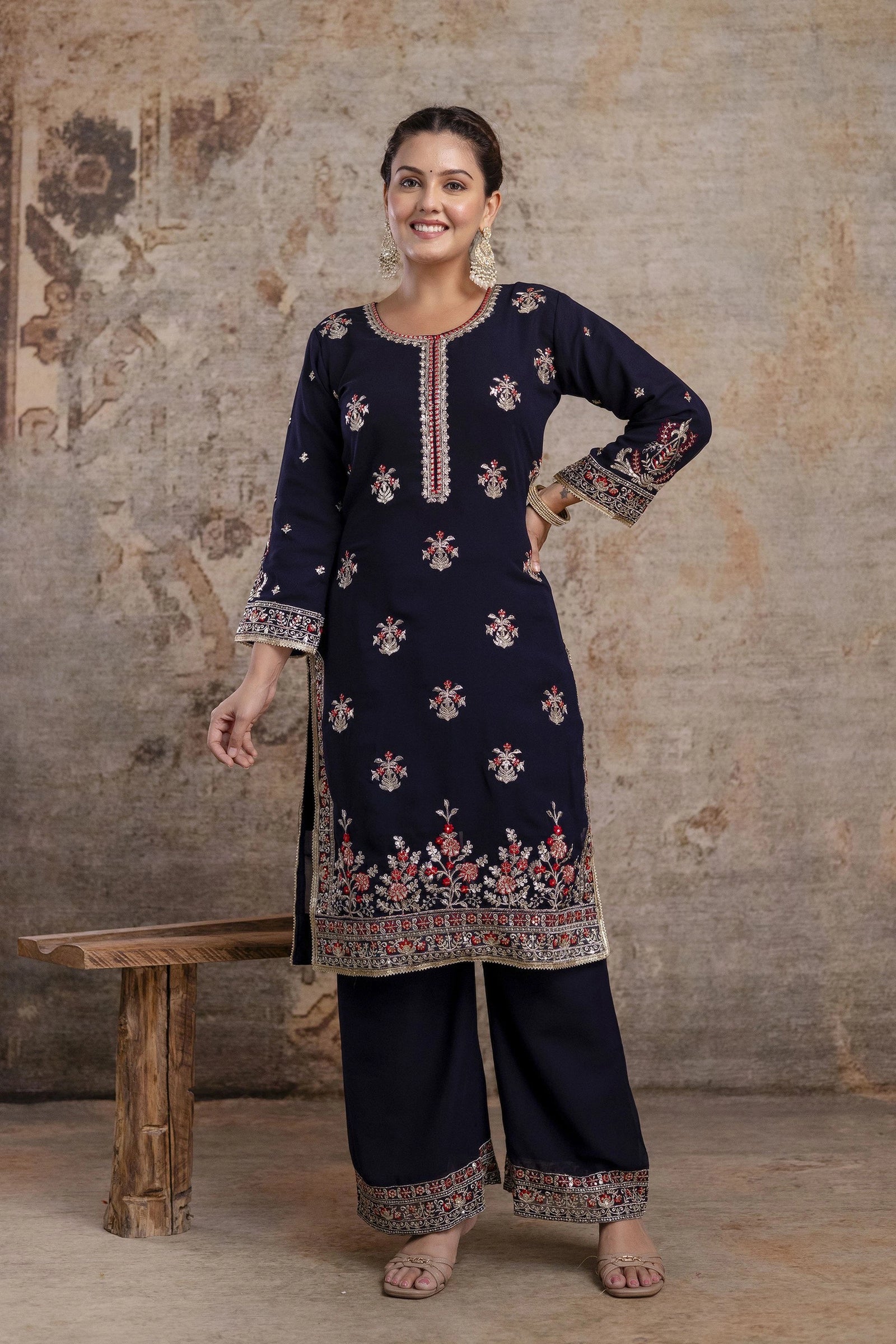 Woman wearing a navy blue embroidered traditional outfit against a textured wall.