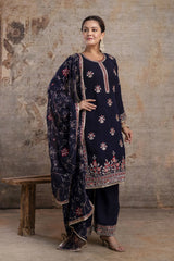 Woman wearing a navy blue embroidered traditional outfit against a textured wall.
