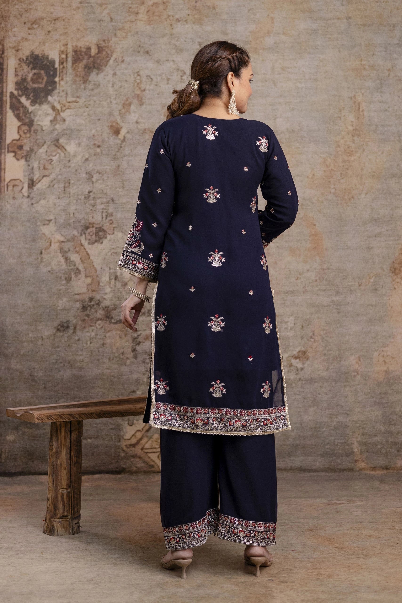 Woman wearing a navy blue traditional outfit with intricate patterns in a rustic setting.
