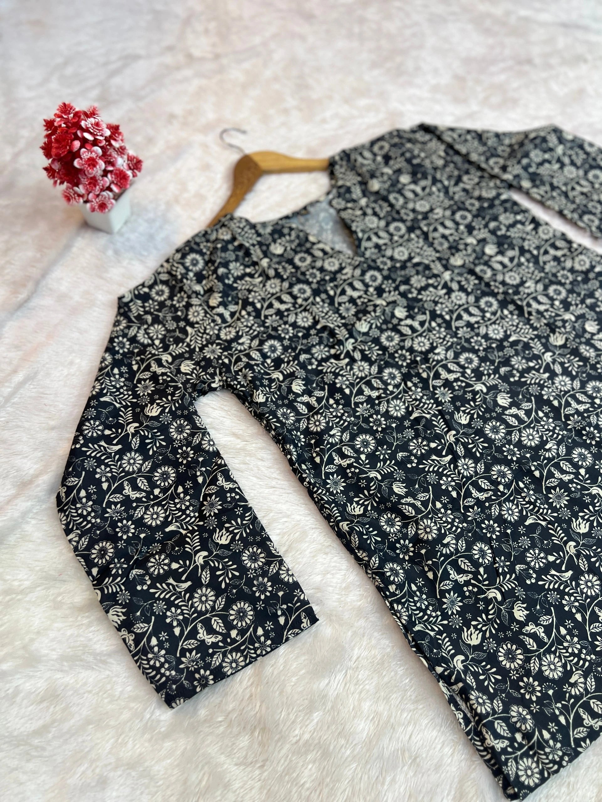 Black floral-patterned shirt on a white surface with a small decorative item.