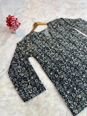 Black floral-patterned shirt on a white surface with a small decorative item.