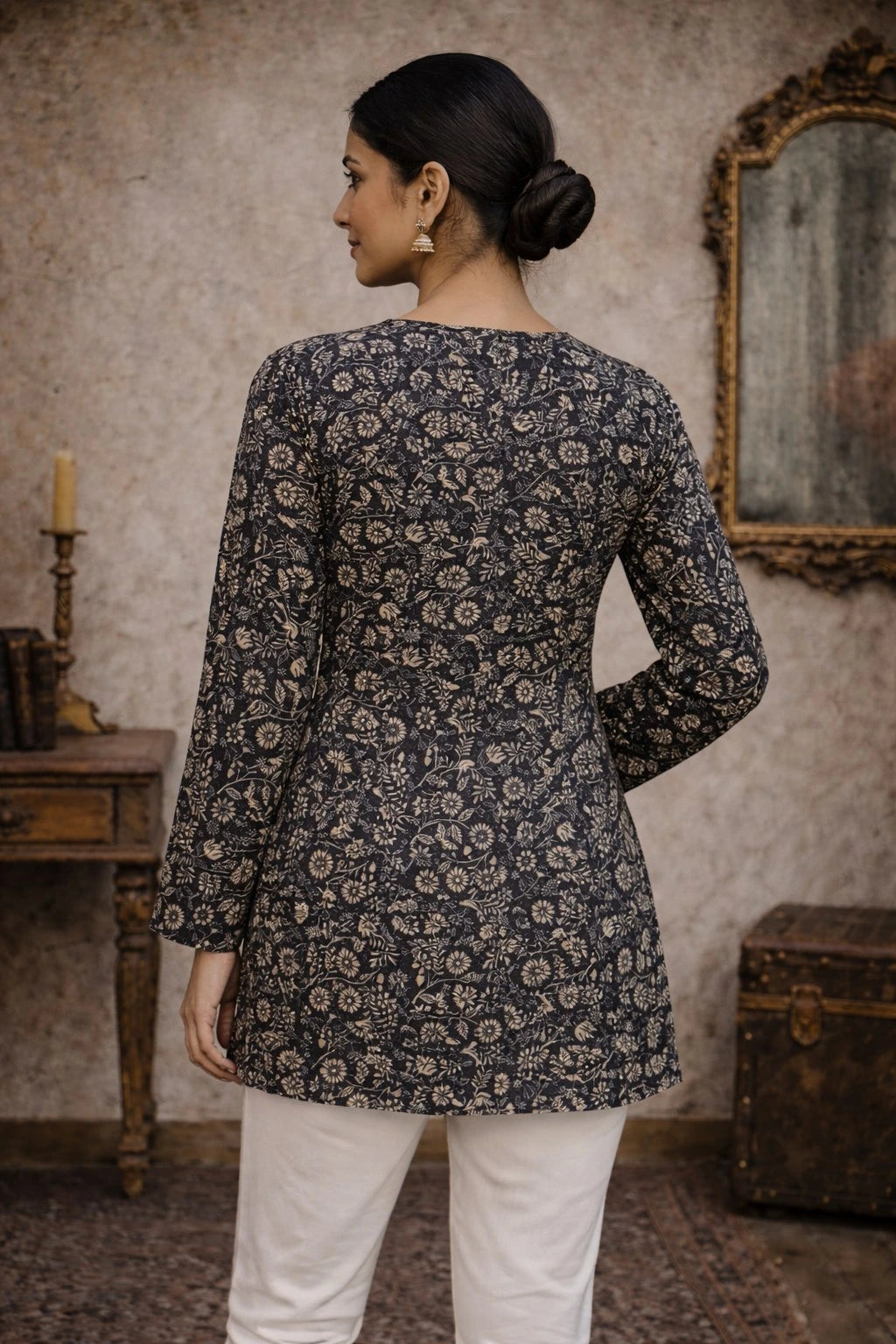 Woman wearing a dark floral patterned top in an indoor setting with a mirror and candle in the background.