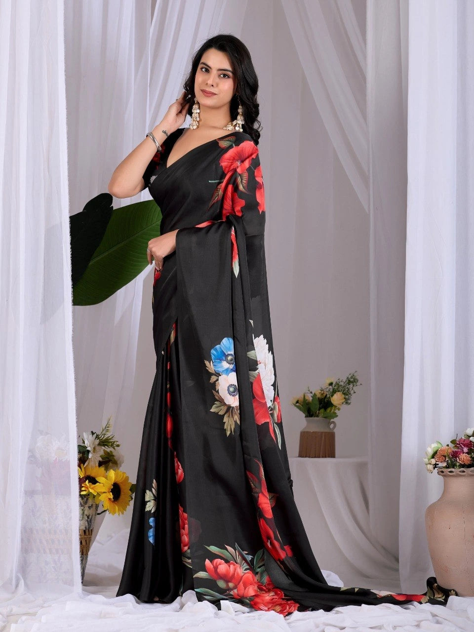 Woman wearing a black saree with floral patterns against a white curtain background