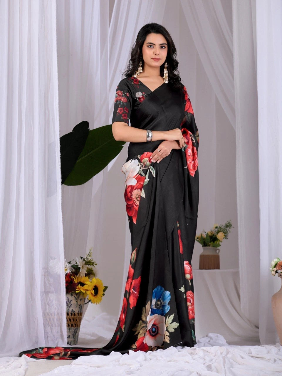 Woman wearing a black saree with floral patterns against a white curtain background