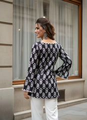 Woman wearing a black and white patterned blouse with white pants standing in front of a building.