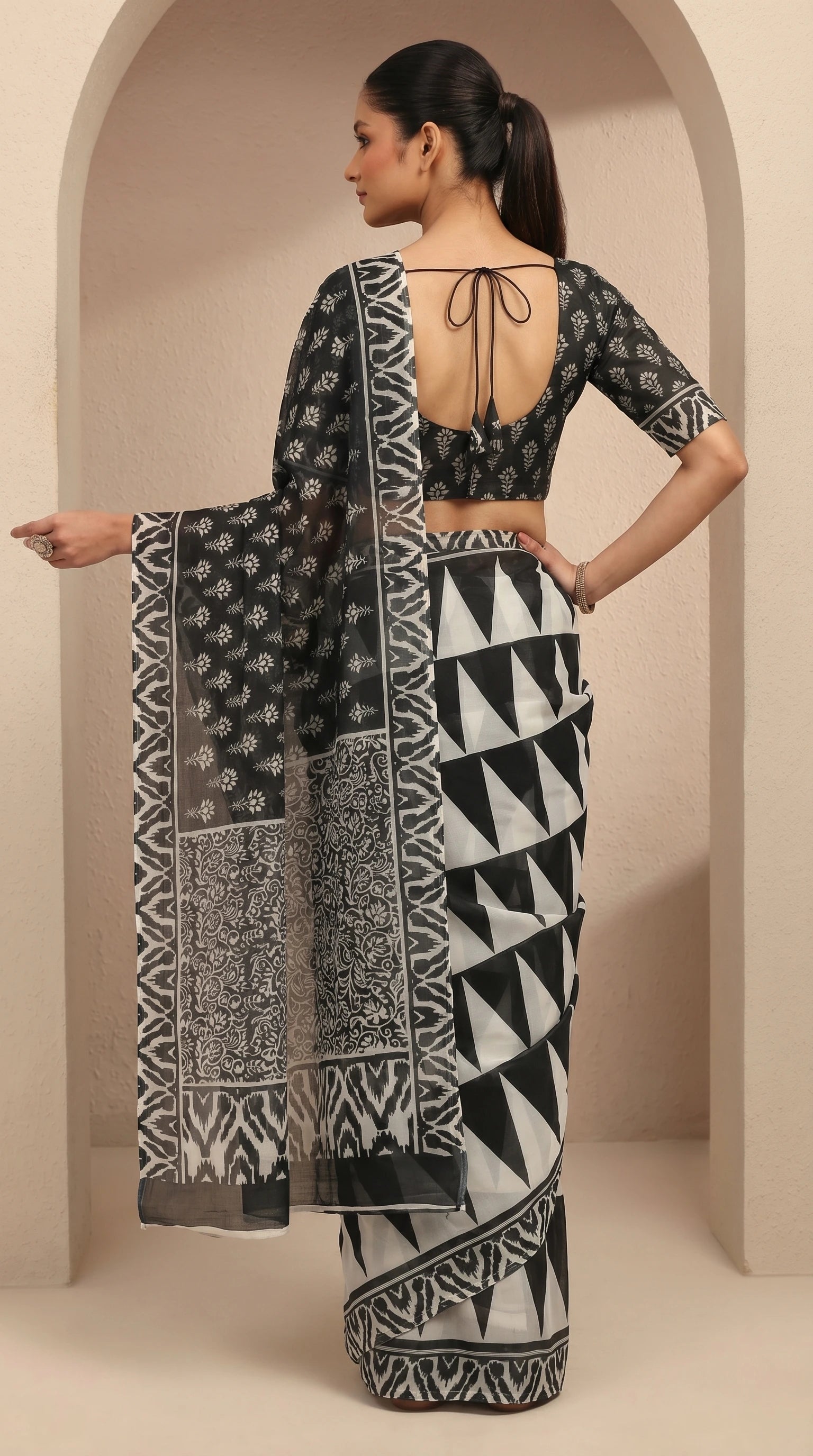 Woman wearing a black and white patterned saree with a matching blouse in a neutral setting.