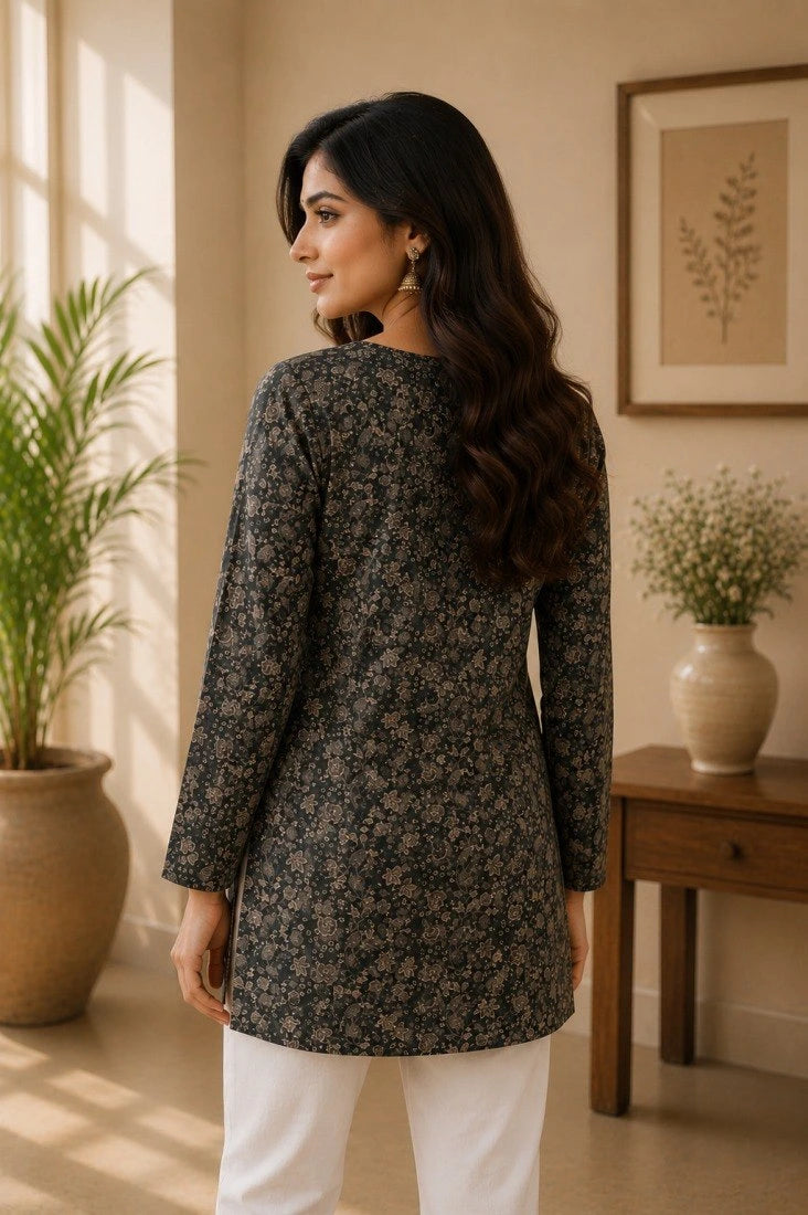 Woman wearing a dark floral long-sleeve top in a room with plants and a table.