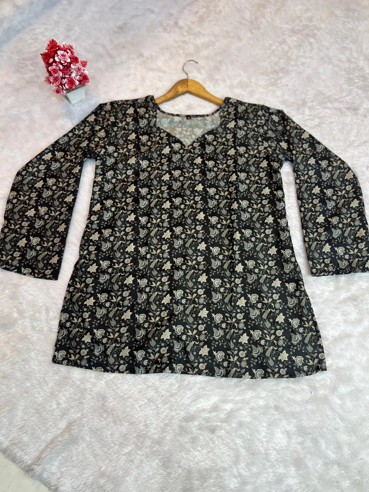 Floral-patterned top on a hanger against a textured white background