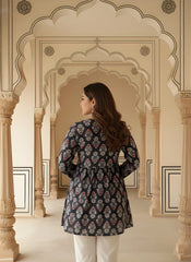 A rear view of the woman showcasing the gathered waistline and the continuous block print across the back of the kurti. She is standing between ornate pillars in a traditional architectural hallway.