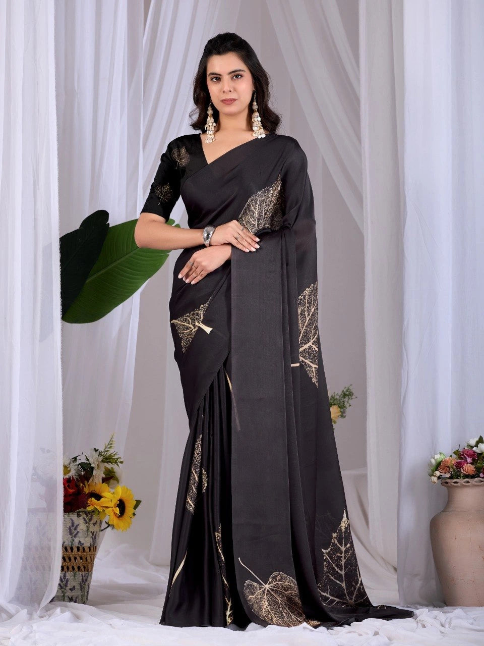 Woman wearing a black saree with gold patterns against a white curtain background
