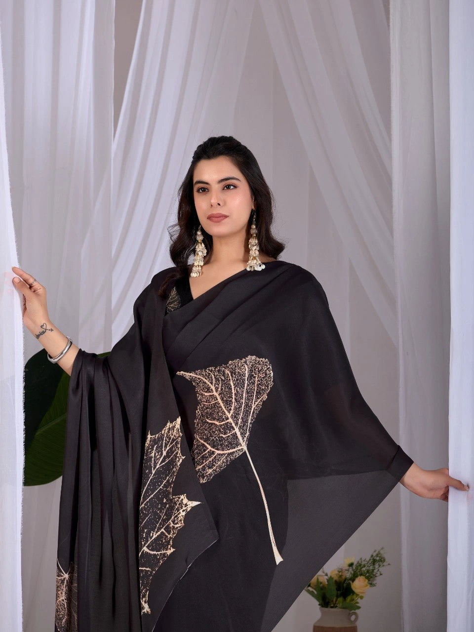Woman wearing a black dress with leaf pattern in front of white curtains