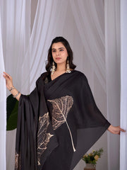 Woman wearing a black dress with leaf pattern in front of white curtains