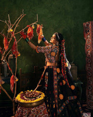 Woman in traditional attire performing a ritual with offerings in a decorated room.
