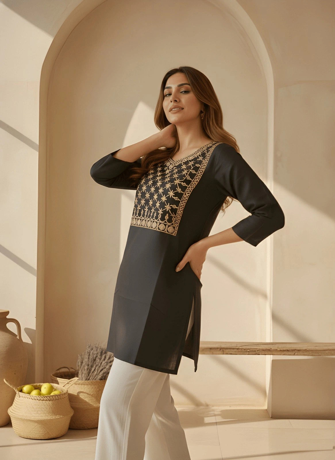 Woman wearing a black and gold embroidered top in a warm-toned interior setting