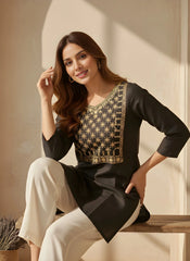 Woman wearing a black and gold embroidered dress sitting on a wooden bench.