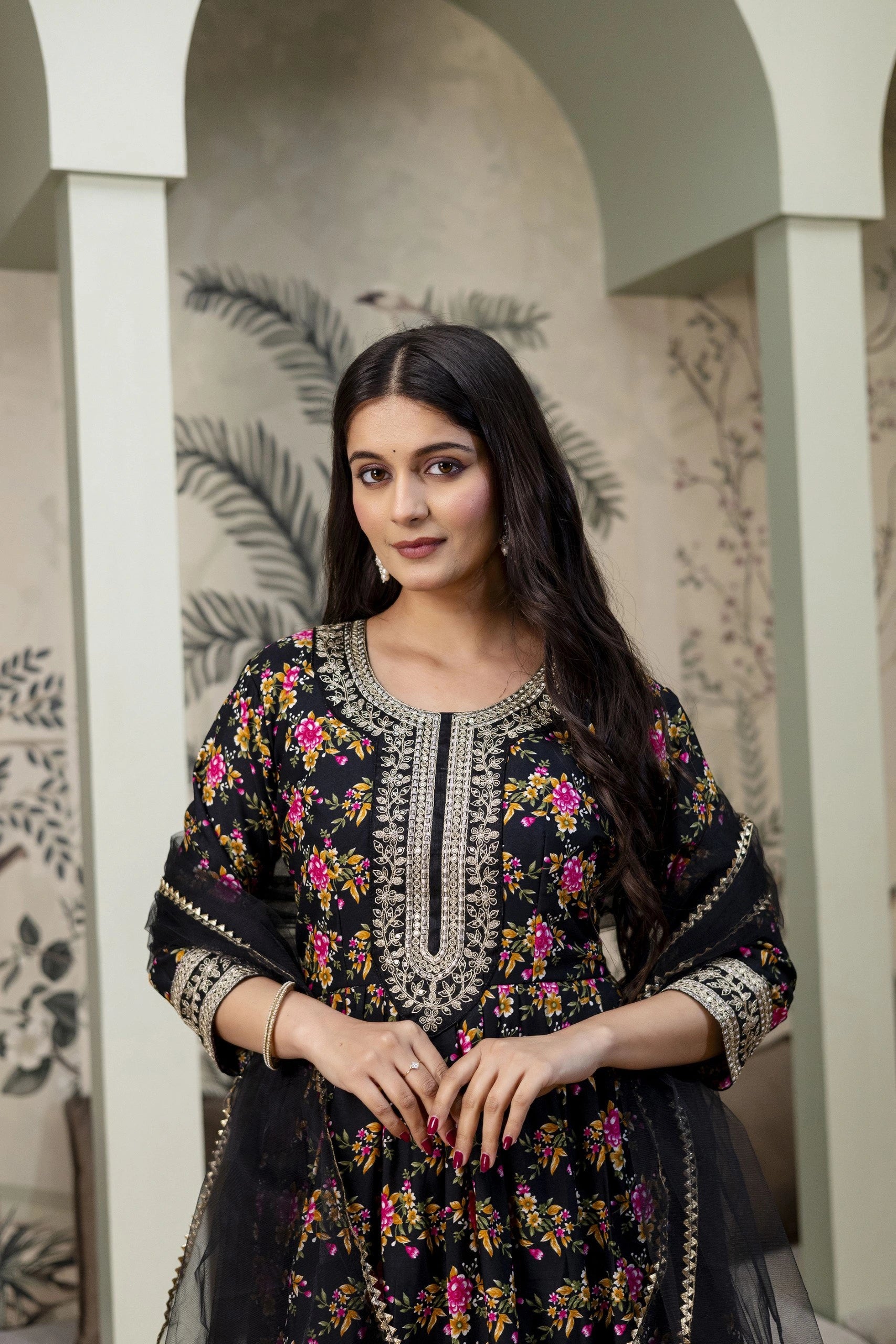 Woman wearing a black embroidered traditional outfit with floral patterns in an indoor setting.