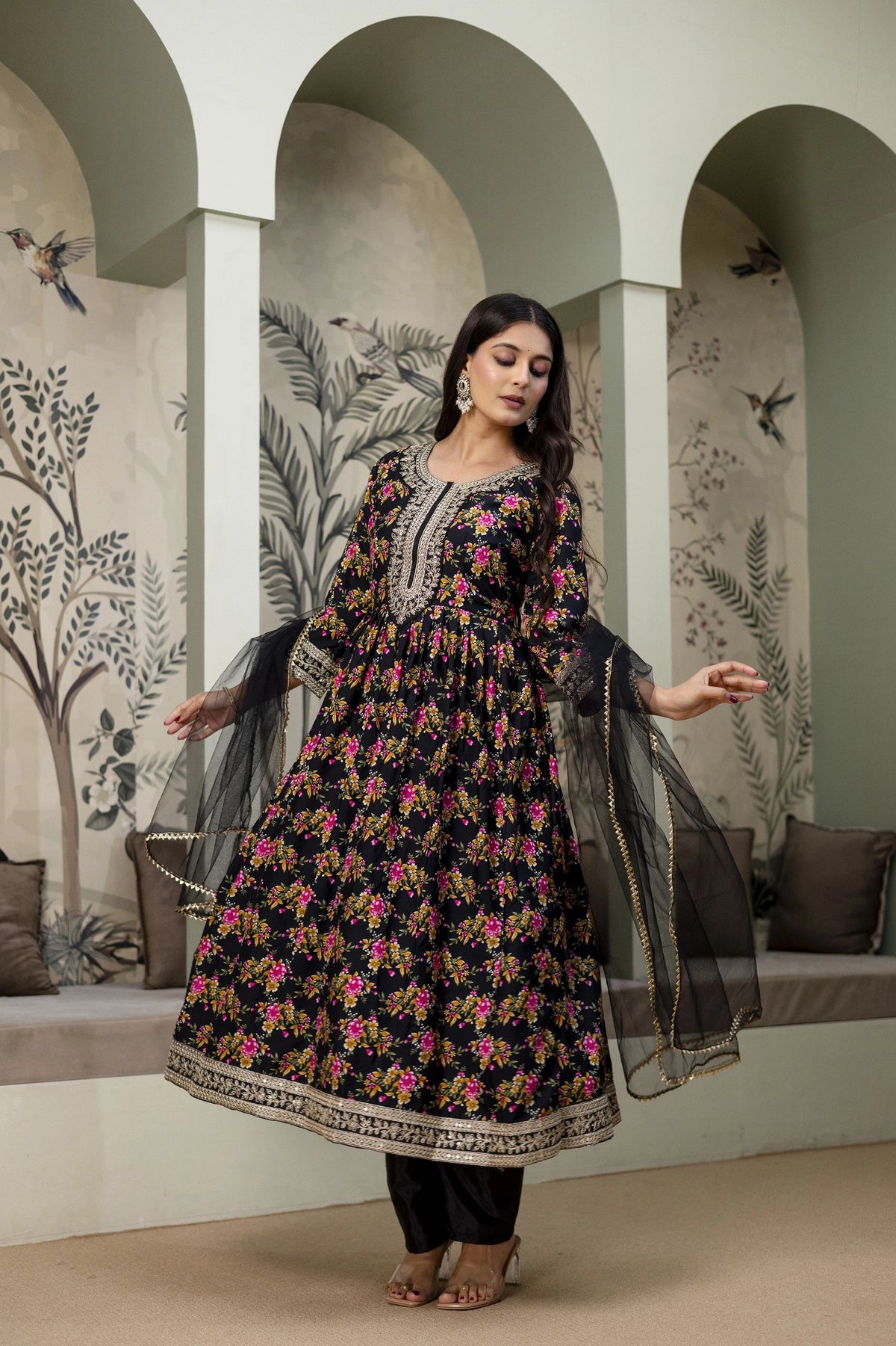 Woman in a floral dress standing in a decorative room with arches and wall art.
