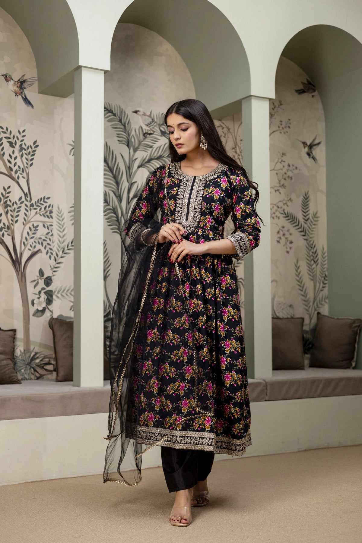 Woman in a floral dress standing in an arched room with decorative walls.