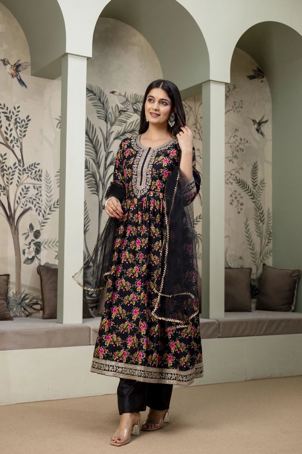 Woman in a floral embroidered dress standing in a decorative interior setting.