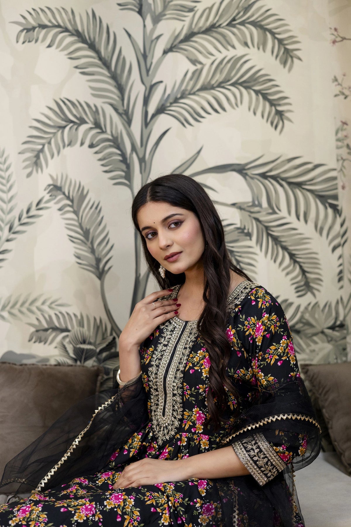 Woman in a floral dress standing against a leaf-patterned wall.