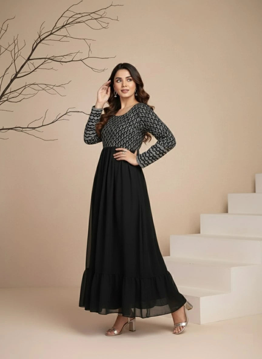 Woman in a black and gray patterned dress standing on a staircase with a beige wall and branch in the background.