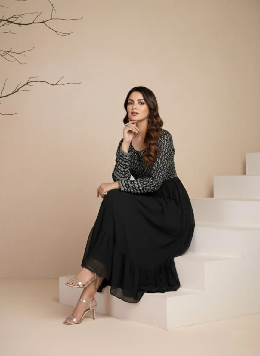 Woman sitting on steps wearing a black and white patterned top and black skirt.