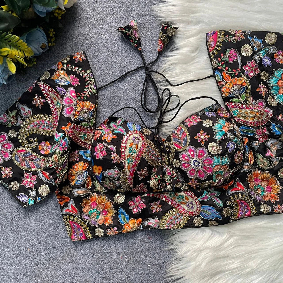 Colorful embroidered top on a textured surface with floral decorations in the background