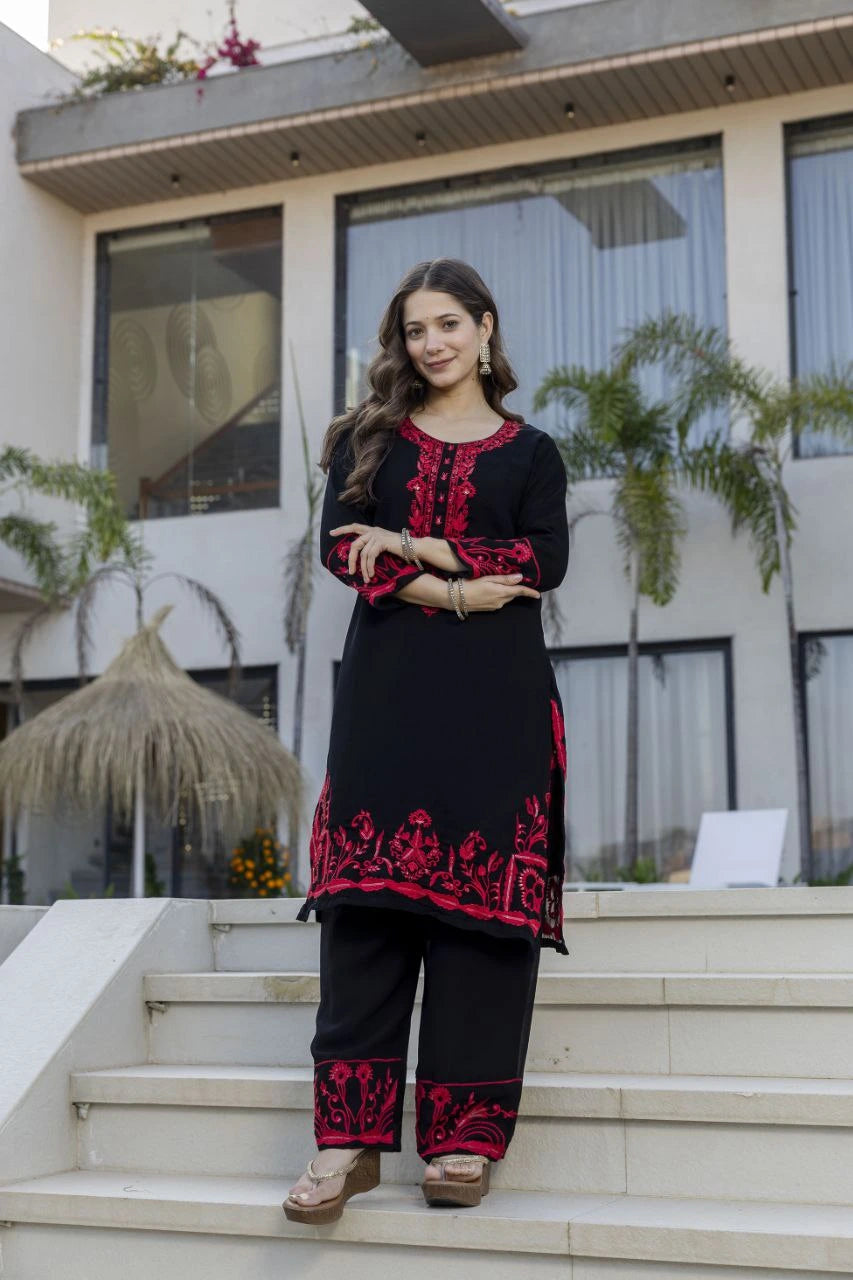 Woman in black and red embroidered outfit standing on steps outside a modern building.