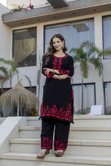 Woman in black and red embroidered outfit standing on steps outside a modern building.