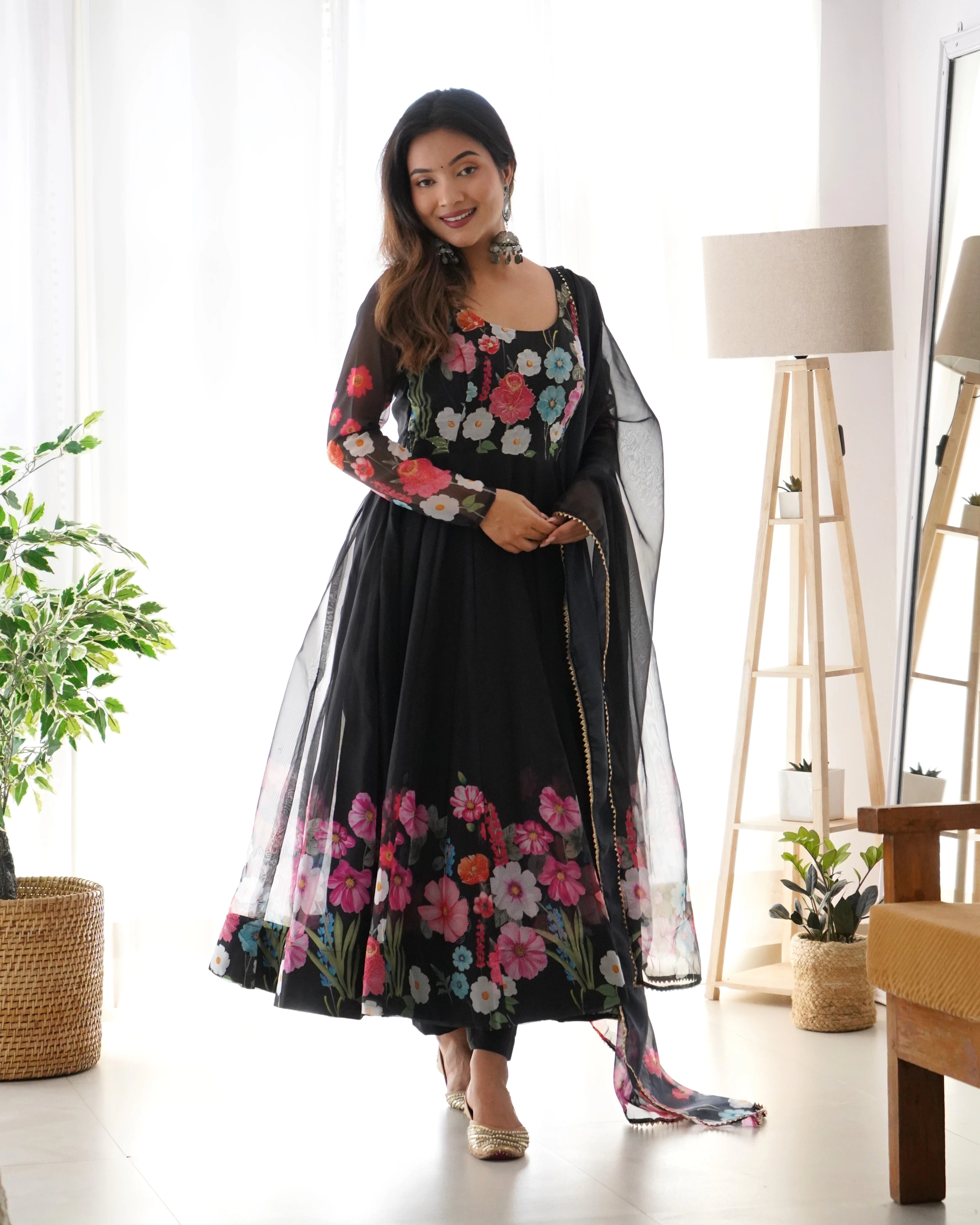 Woman wearing a black floral dress with a sheer overlay in a bright room.