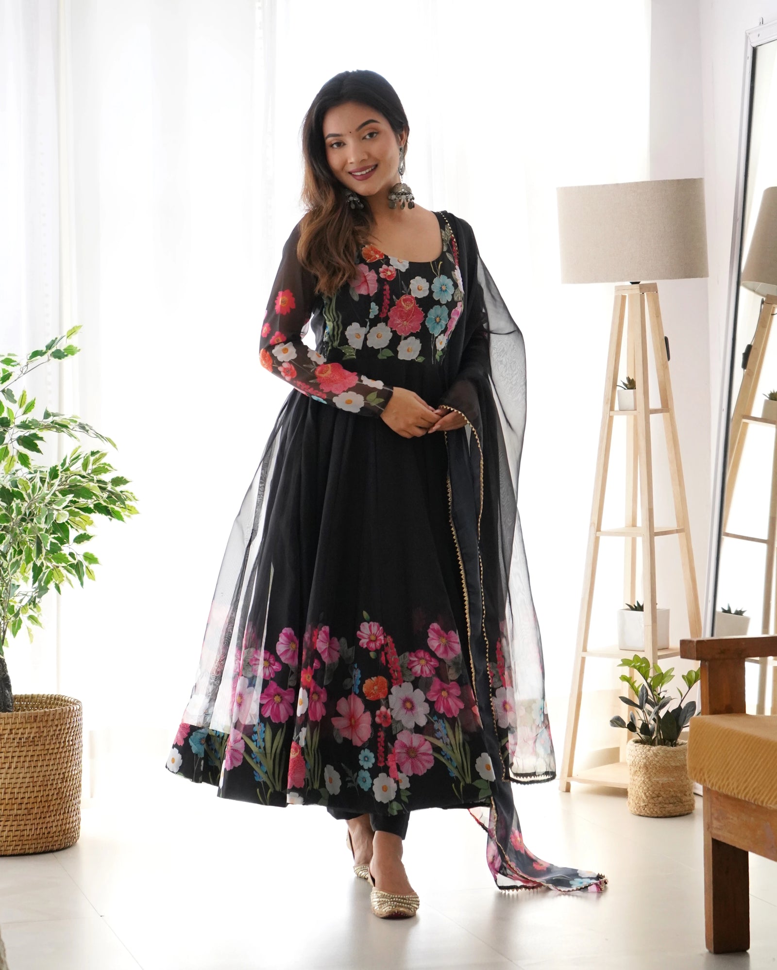 Woman wearing a black floral dress with a sheer overlay in a bright room.