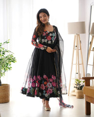 Woman wearing a black floral dress with a sheer overlay in a bright room.
