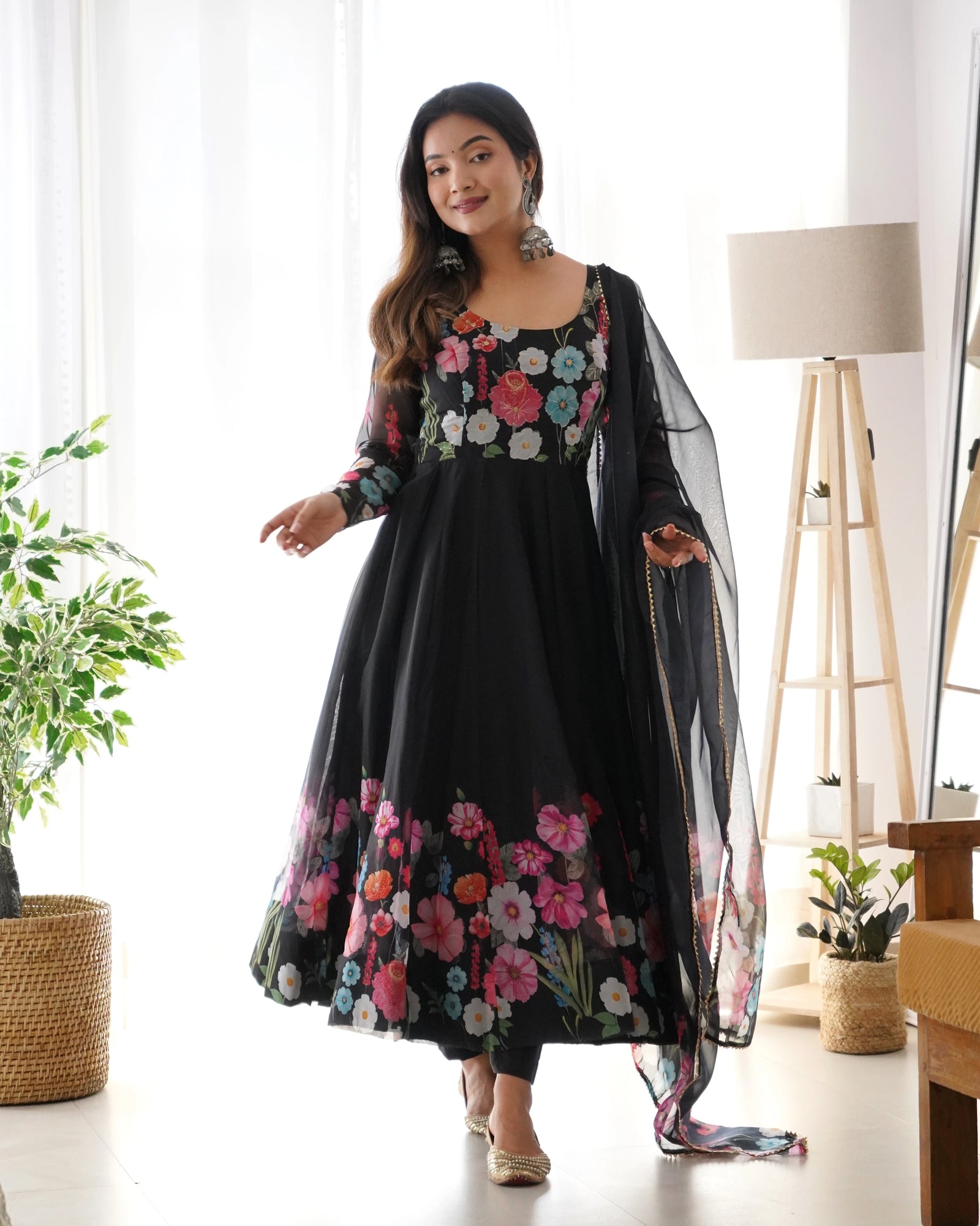 Woman wearing a black floral dress with a sheer dupatta in a bright room.