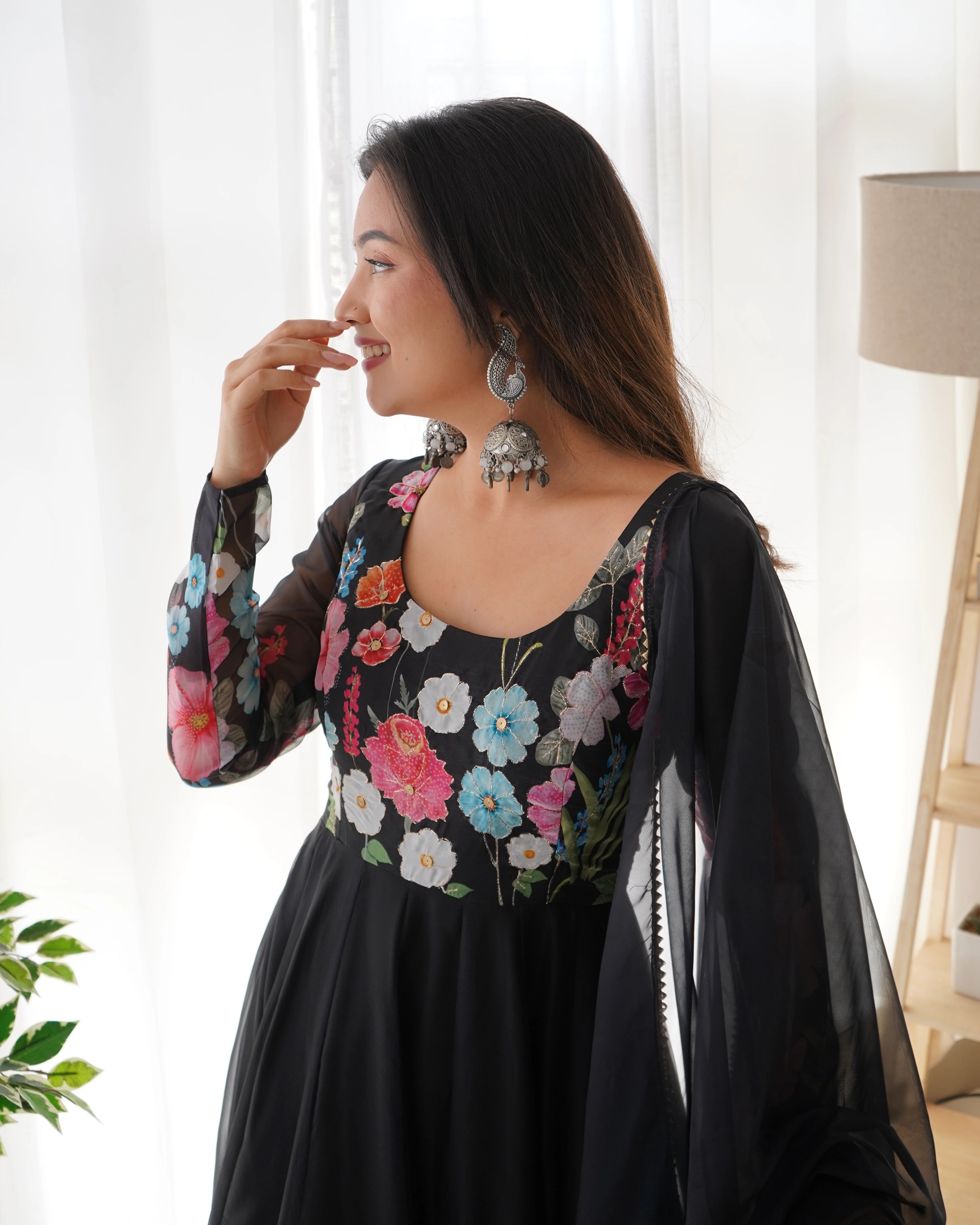 Woman wearing a black floral dress in a bright room with white curtains.