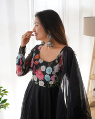 Woman wearing a black floral dress in a bright room with white curtains.