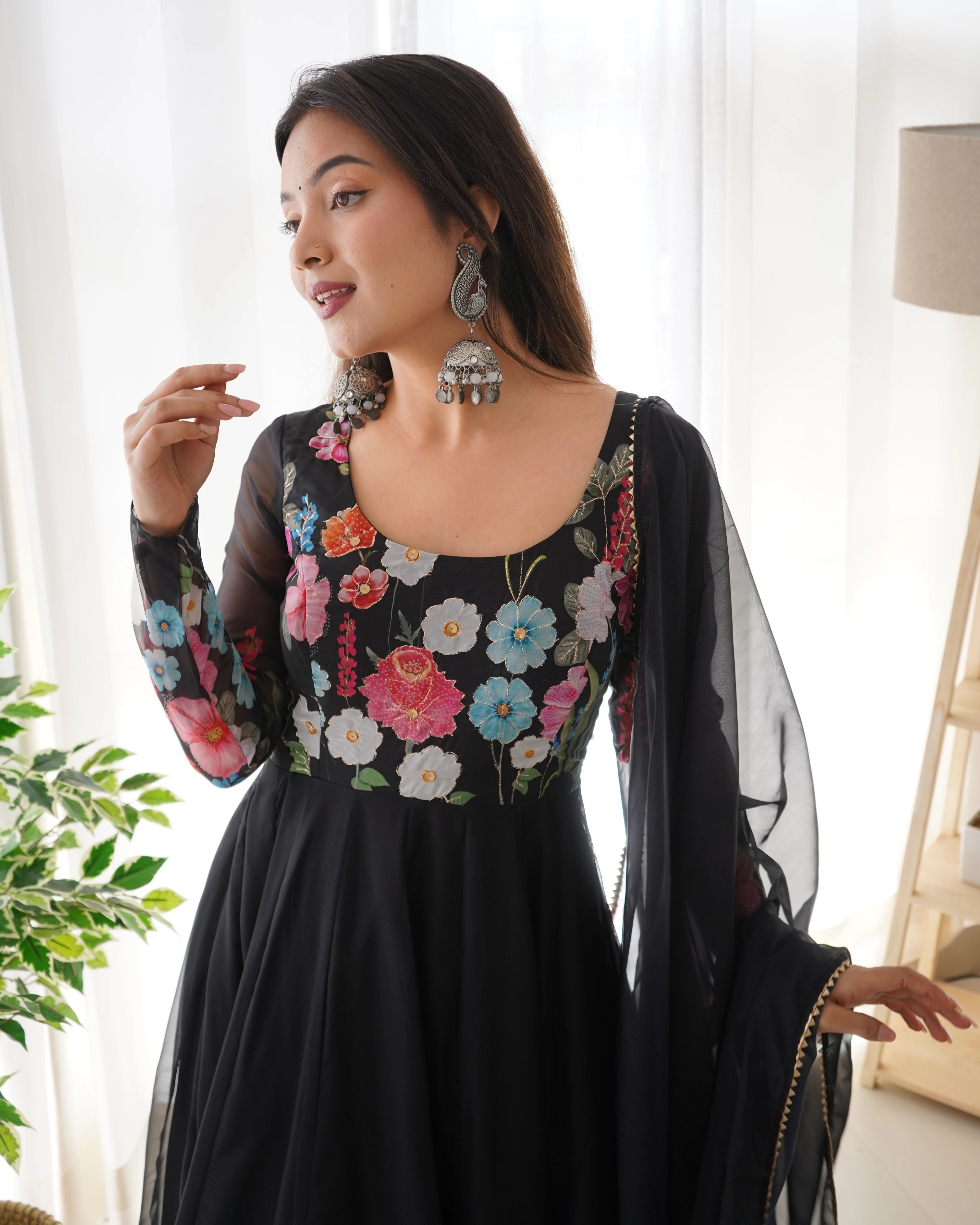 Woman wearing a black dress with colorful floral embroidery indoors.