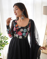 Woman wearing a black dress with colorful floral embroidery indoors.