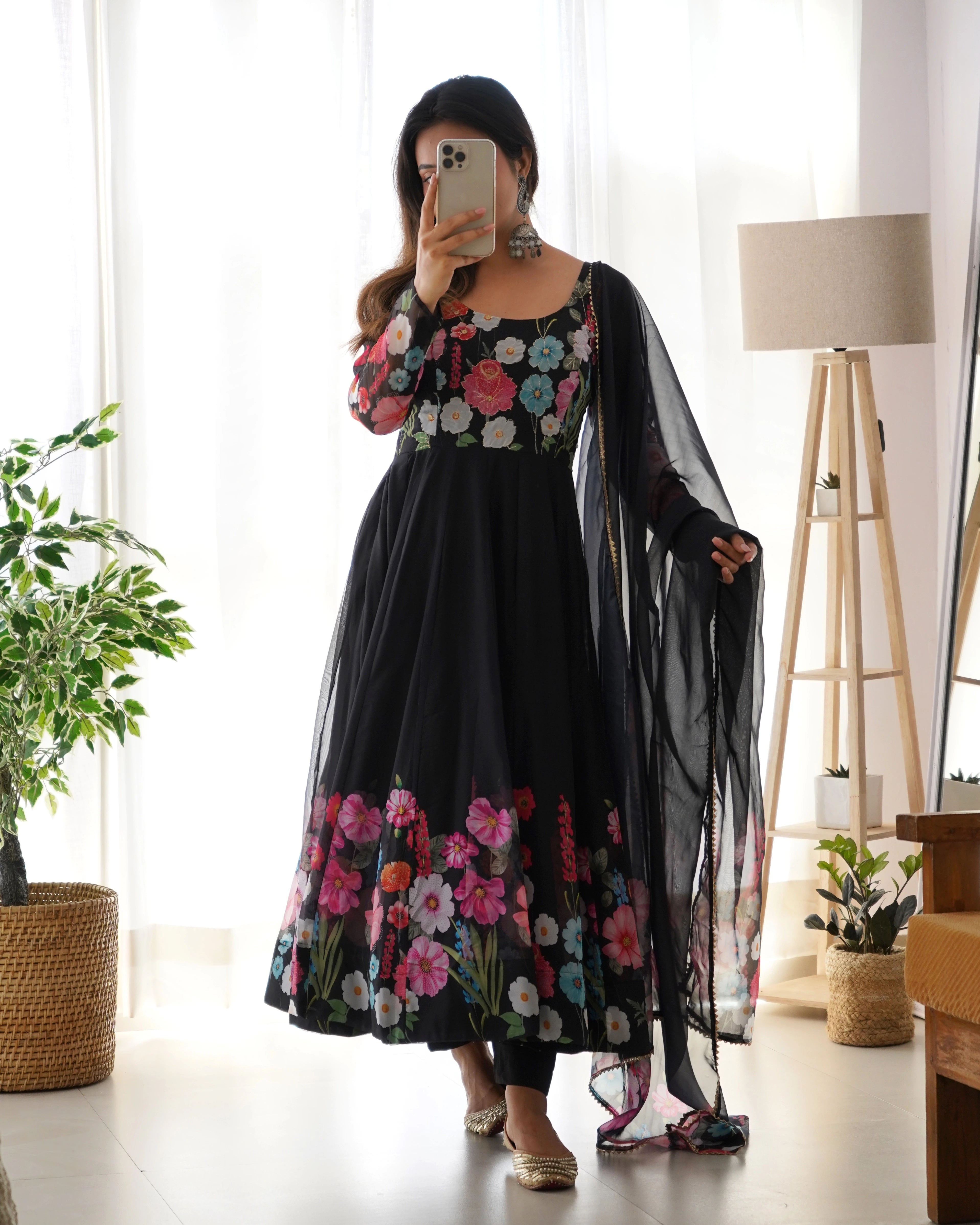 Woman wearing a black floral dress in a room with a plant and lamp.