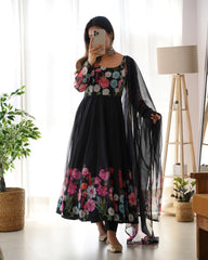 Woman wearing a black floral dress in a room with a plant and lamp.