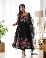Woman wearing a black floral dress with a sheer dupatta in a bright room.