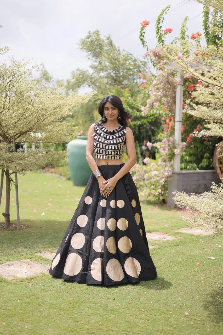Elegant black lehenga choli featuring a sleeveless mirror work blouse and a flared skirt with bold golden polka dot motifs.