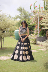 Elegant black lehenga choli featuring a sleeveless mirror work blouse and a flared skirt with bold golden polka dot motifs.
