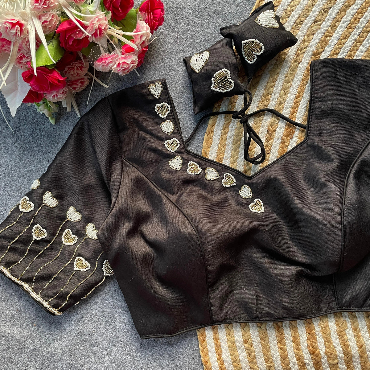 Black blouse with gold heart embroidery on a textured surface with flowers.