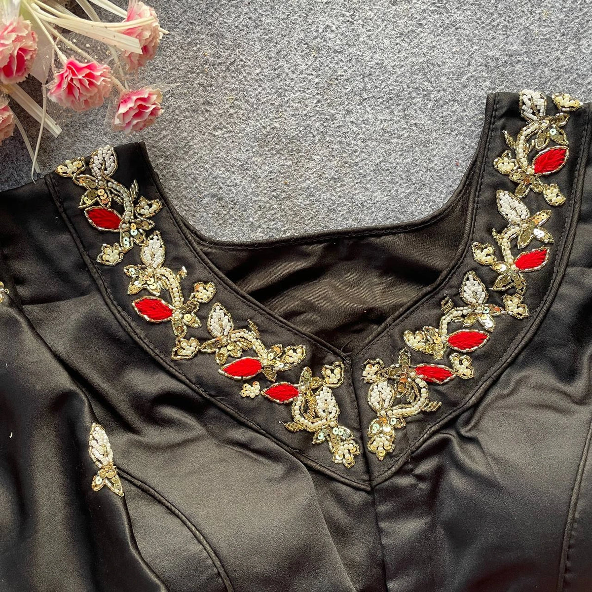 Black blouse with gold and red embroidery on a textured gray background